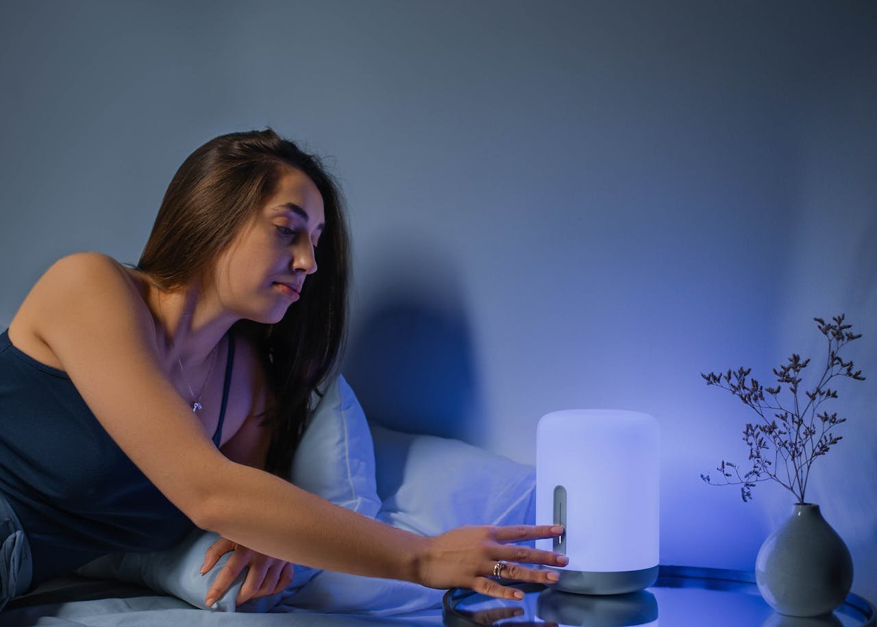 A woman in a cozy bedroom adjusts a modern bedside lamp for ambient lighting.